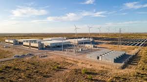 An aerial view of a data center beside wind turbines and a solar array on flat open land