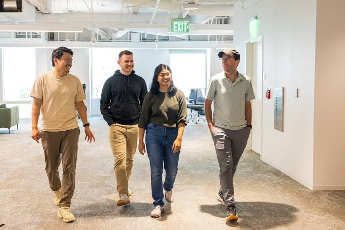 Four people walking through an open-plan technology office, representing the teams behind AI training-data startups