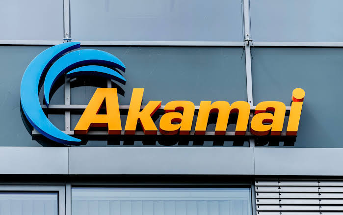 The Akamai logo in orange lettering with a blue wave mark on the glass facade of an Akamai office building