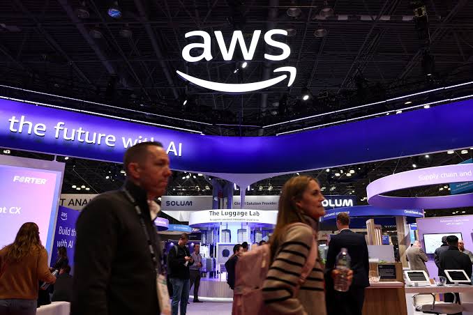 Visitors walk beneath a large AWS logo and a banner reading the future with AI at an Amazon Web Services exhibition stand