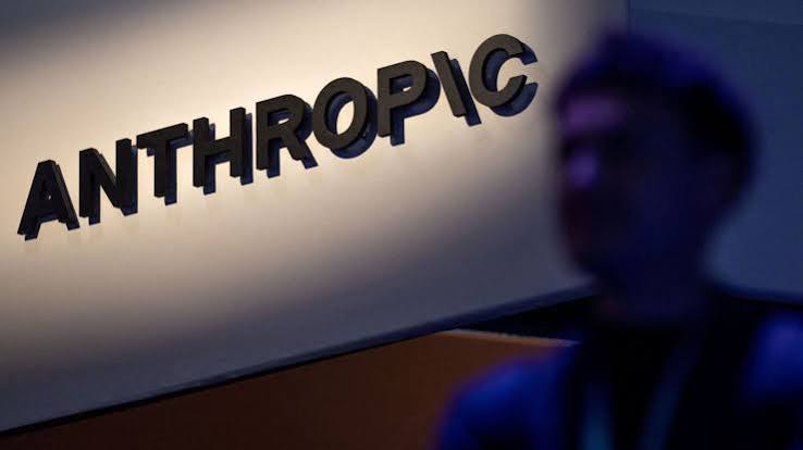 Anthropic company logo in black letters on a lit wall, with a blurred figure in the foreground