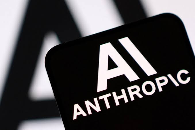 A smartphone displaying the Anthropic AI logo in white on a black screen, with the Anthropic wordmark on the wall behind it