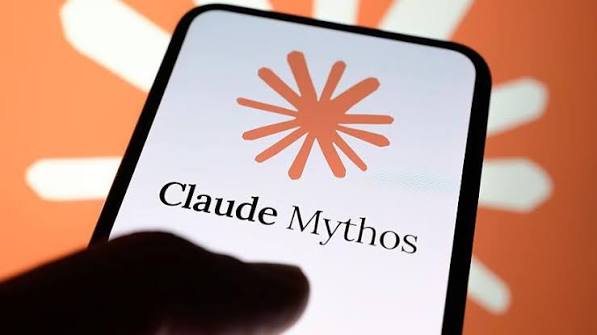 A hand reaching toward a smartphone displaying the Claude Mythos logo, an orange starburst above the words Claude Mythos, against an orange background