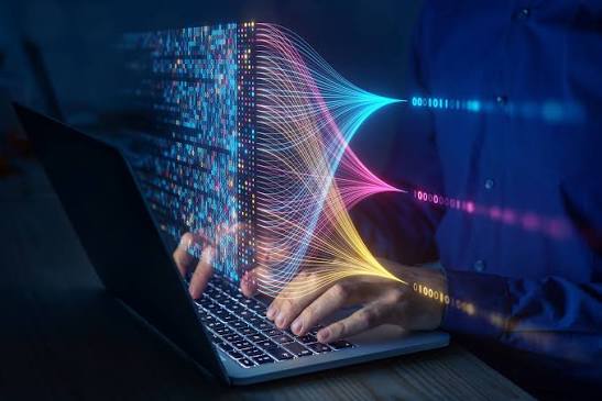 Hands typing on a laptop with streams of colored data flowing from the screen