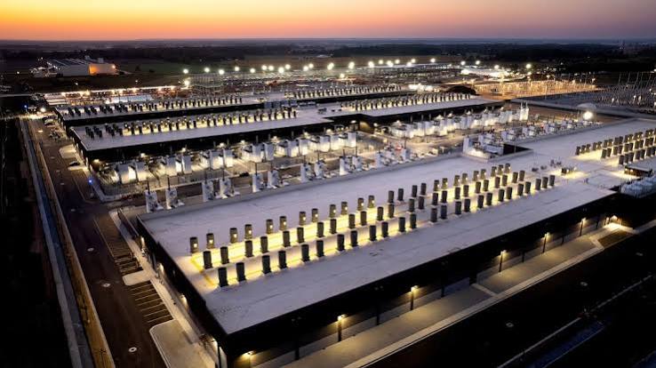 Aerial view at dusk of a large data center campus with rows of rooftop cooling units and lit buildings