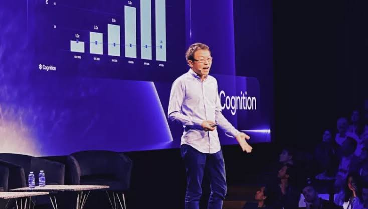 A Cognition executive presents on stage in front of a rising revenue bar chart, with the Cognition logo behind