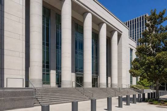 A modern federal courthouse with tall stone columns and a glass facade, with wide entrance steps under a blue sky