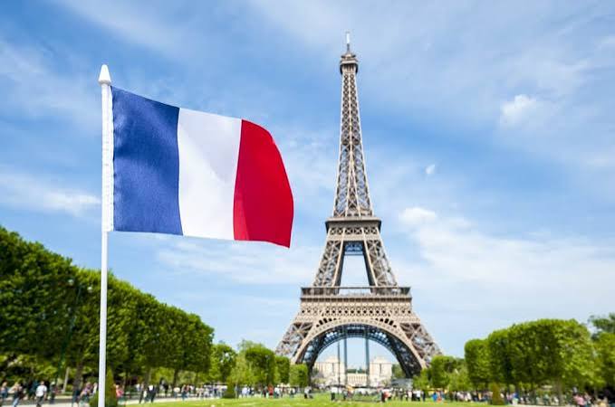 A French tricolor flag flying beside the Eiffel Tower in Paris under a blue sky