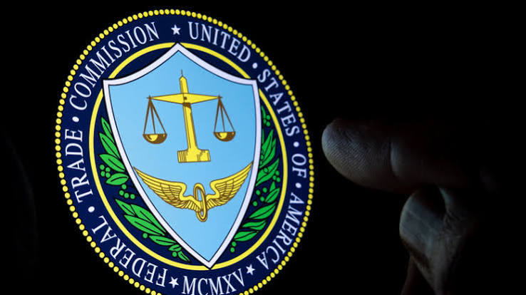 The seal of the US Federal Trade Commission glowing against a dark background, with a hand reaching toward it