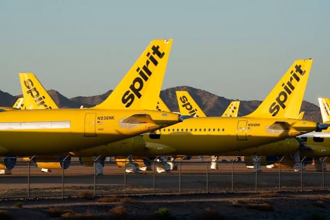 Yellow Spirit Airlines jets parked in a desert storage lot, their tails marked spirit, with mountains in the background