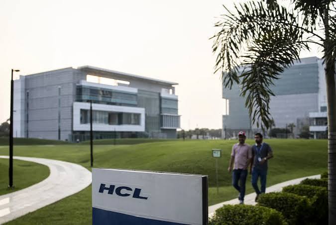 HCL sign in front of a modern HCLTech office campus in India with employees walking along a landscaped path