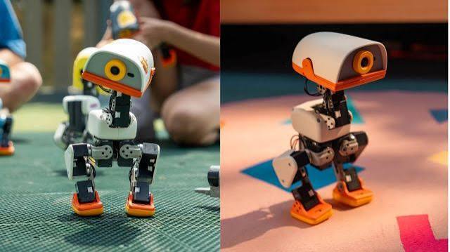 Two views of the Microduck, a small white, black and orange open-source bipedal robot with a single round camera eye, standing on a play mat