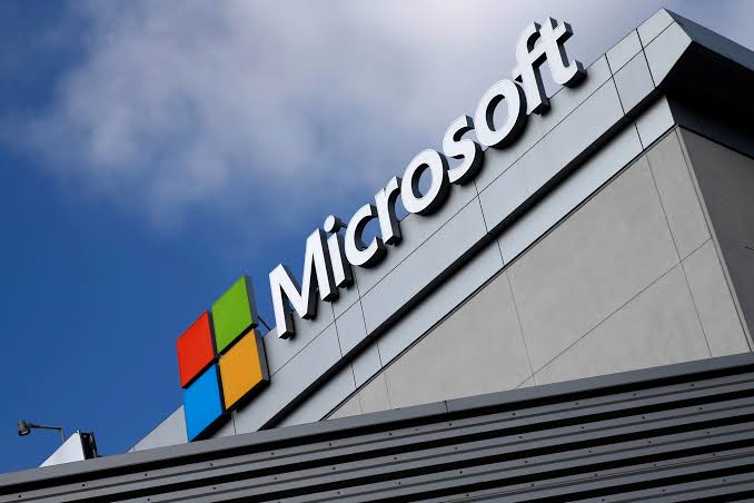 Microsoft logo and wordmark on the roof edge of an office building against a blue sky