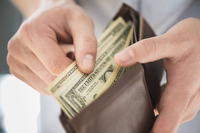 Hands counting US dollar bills from an open brown leather wallet