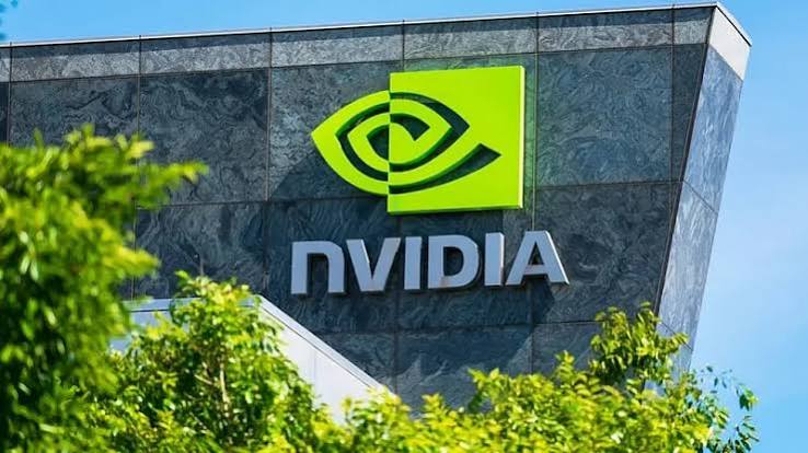 The green Nvidia logo and wordmark on the stone facade of the company's headquarters, framed by green foliage and blue sky