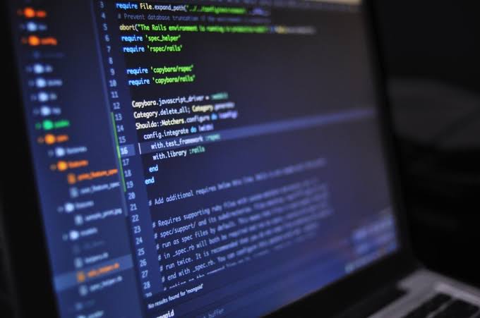 A laptop screen at an angle showing colorful lines of programming code in a dark editor