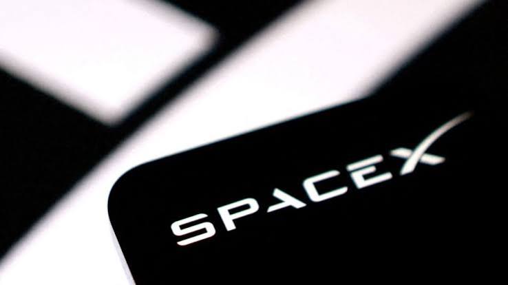 Close-up of the SpaceX logo in white on a black card against a blurred black and white background