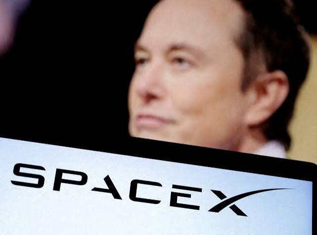 SpaceX logo on a screen in front of a blurred photo of Elon Musk