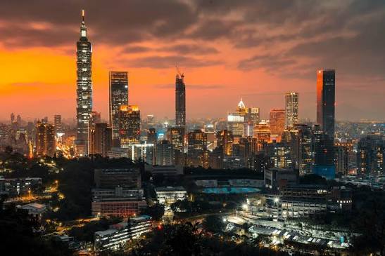 The Taipei skyline at dusk with Taipei 101 rising above the city under an orange sunset sky