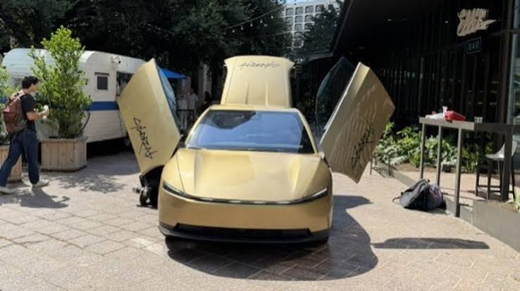 A gold Tesla Cybercab robotaxi with its gull-wing doors open, parked on an Austin plaza