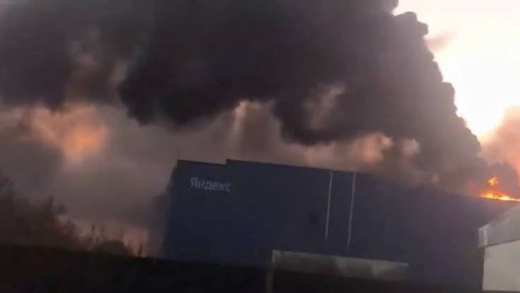 Thick black smoke and flames rising above a blue Yandex-branded data center building at dusk